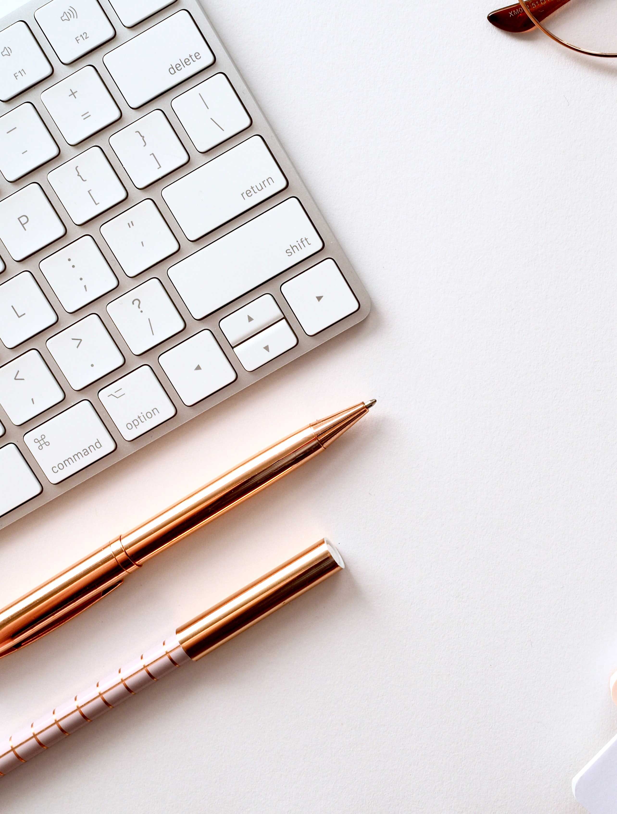 Computer keyboard, pens, glasses and notepads on a desk